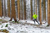 Ein Jogger in neongelbgrüner Fitnessjacke und Kappe joggt durch den verschneiten Wald Ein Jogger in neongelbgrüner Fitnessjacke und Kappe joggt durch den verschneiten Wald